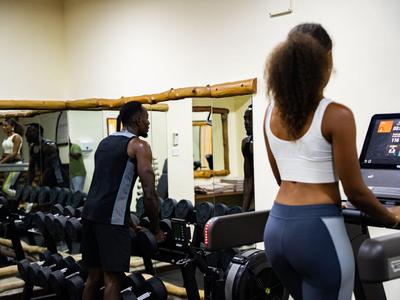 Zwei Personen nutzen Geräte im Hotel-Fitnessstudio mit Spiegel und Hanteln.