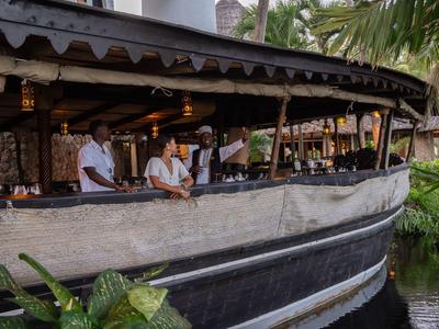 Mehrere Kellner im offenen, holzverkleideten Restaurantboot an einem tropischen Ort.