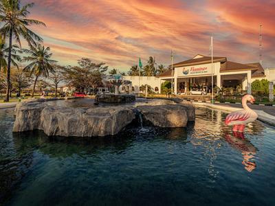 Luxuriöser Pool mit Felseninsel, Flamingo-Schwimminsel und Palmen bei orangefarbenem Sonnenuntergang.
