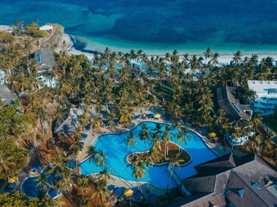 Blick auf Palmen, mehrere Pools und weißen Sandstrand mit türkisblauem Meer im Hintergrund.