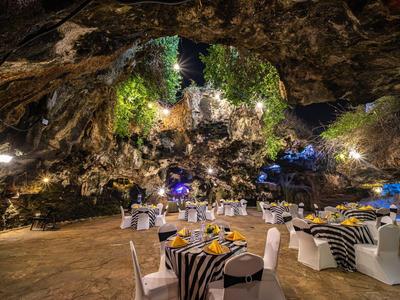Heller Festsaal mit runden Tischen, schwarzen Tischdecken, weißen Stühlen in großer Höhle mit Pflanzen.