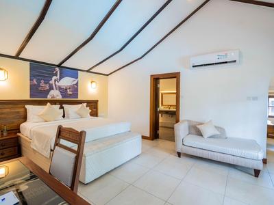 Brightly furnished bedroom with double bed, sofa, air conditioning, and bathroom in the background.
