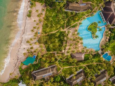 Aerial view of a beachfront resort with multiple buildings, pools, and abundant greenery.