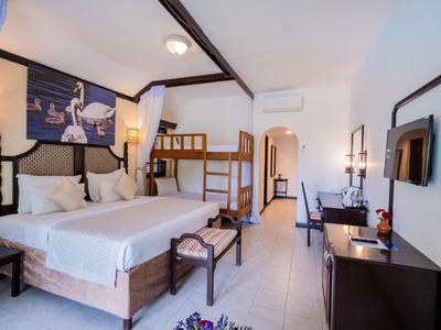 Bright hotel room with double bed, bunk bed, desk, and mirror.