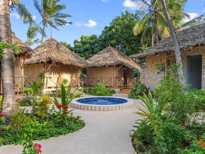 Small stone huts surrounded by tropical vegetation with a round pool in the center.