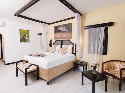 Brightly decorated hotel room with canopy bed, seating area, and artwork on walls.