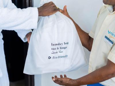 Hotel staff hand over an eco-friendly laundry bag to a guest wearing a bathrobe.