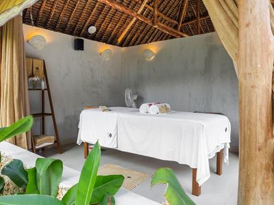 Bright massage room with wooden roof, white massage table, and green plants in the foreground.