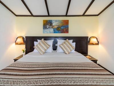 Gemütliches Schlafzimmer mit großem Bett, gemusterten Kissen, Wandlampen und buntem Bild.