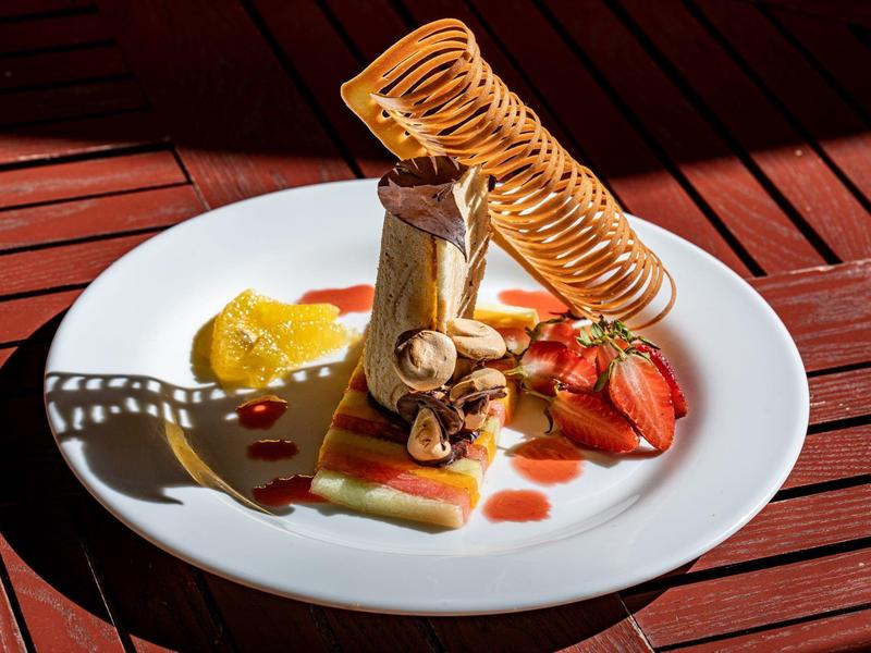 Kunstvoll angerichtetes Dessert mit Bananen, Erdbeeren, Karamellspirale und Fruchtsauce auf weißem Teller.