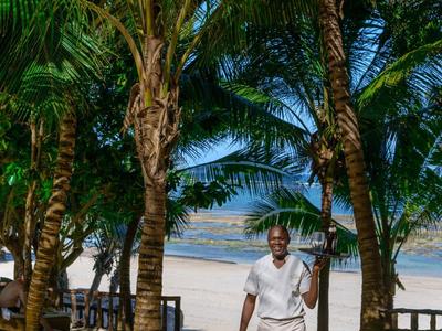 Personnes se détendant sur des chaises longues près de la piscine avec arbres et mer en arrière-plan.
