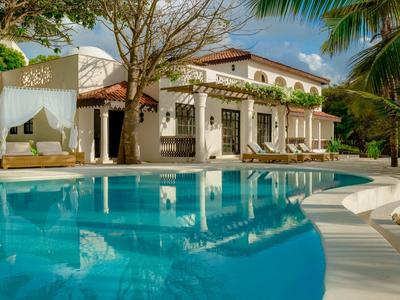 Villa de luxe avec piscine et chaises longues, entourée de palmiers et d'arbres en fleurs.