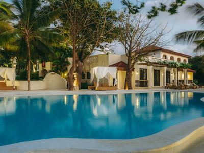 Hôtel tranquille avec piscine et palmiers en soirée sous un ciel nuageux.