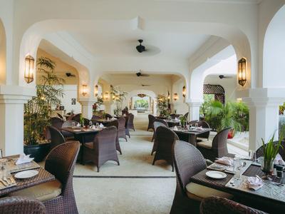 Espace de restaurant ouvert avec tables dressées et chaises en rotin sous de grandes arches.
