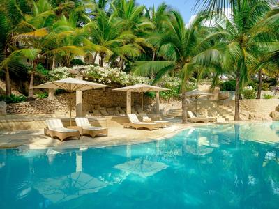 Einladender Pool mit blauer Wasserfläche, umgeben von Palmen und beigen Liegen unter Sonnenschirmen.