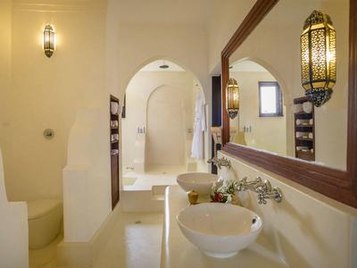 Salle de bain lumineuse avec lavabo rond, grand miroir et baignoire sous une arche.