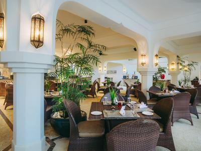 Restaurant élégant et lumineux avec des chaises en osier, des plantes et des tables dressées sous des arches.