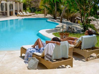 Deux personnes se détendent sur des transats au bord d'une piscine dans un cadre hôtelier ensoleillé.