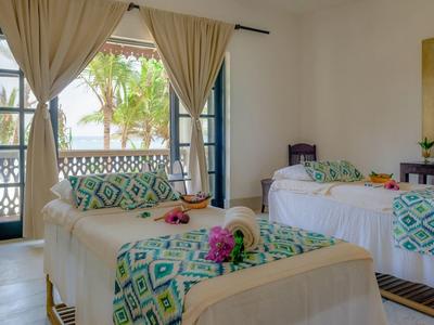 Chambre d'hôtel lumineuse avec deux lits, coussins à motifs et rideaux.