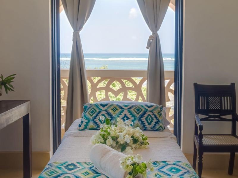 Lit de chambre d'hôtel avec vue sur balcon et mer à travers une fenêtre avec rideaux