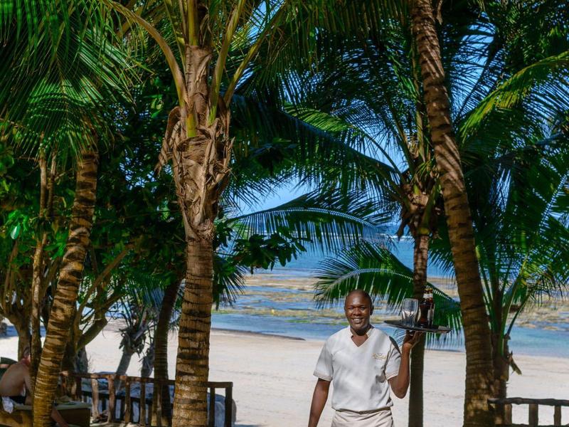 Personnes se détendant sur des chaises longues près de la piscine avec arbres et mer en arrière-plan.