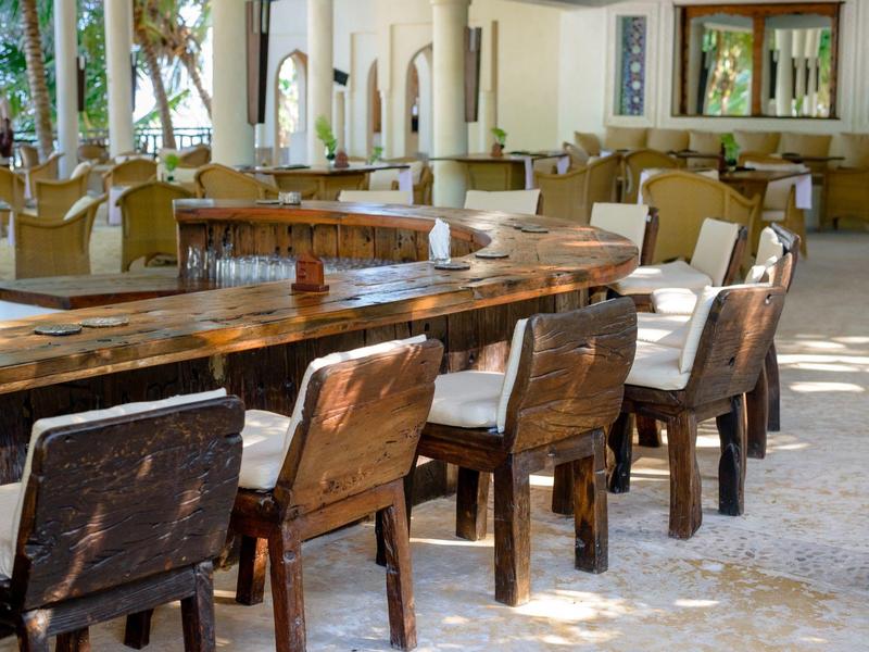 Grande salle à manger avec table en bois courbée et de nombreuses chaises dans un espace lumineux et ouvert.