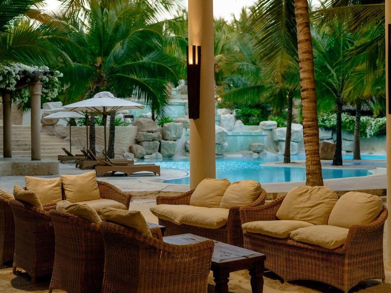 Coin salon confortable sur la terrasse de l'hôtel avec vue sur la piscine tropicale.