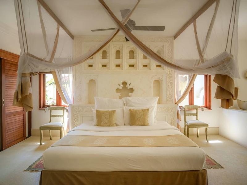 Chambre lumineuse avec grand lit, moustiquaire et tons neutres chauds.