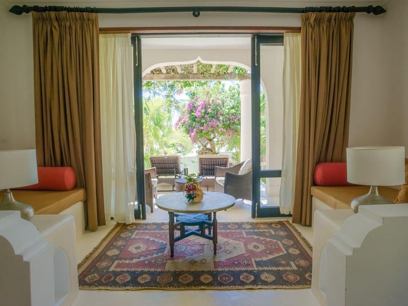 Chambre confortable avec canapés, tapis et vue sur une terrasse avec coin salon et jardin.