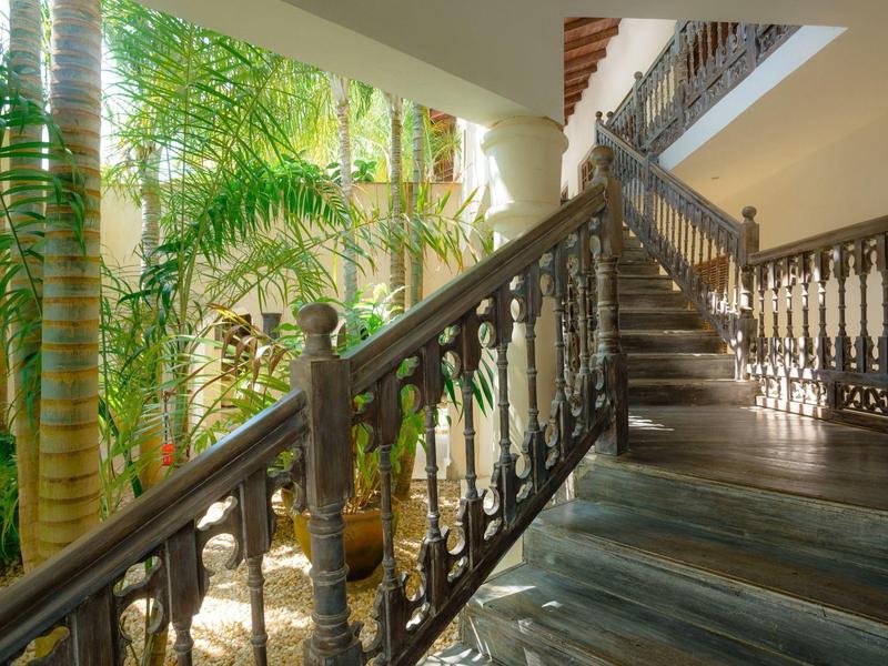 Grand escalier avec rambarde en fer forgé et plantes tropicales dans la cour intérieure.