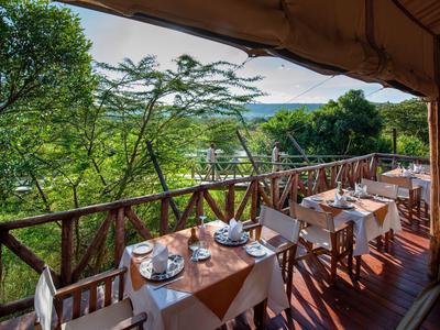 Terrasse eines Hotels mit gedeckten Tischen und Blick auf grüne Bäume und Himmel.