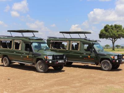 Zwei grüne Safari-Geländewagen stehen auf staubigem Gelände unter blauem Himmel.