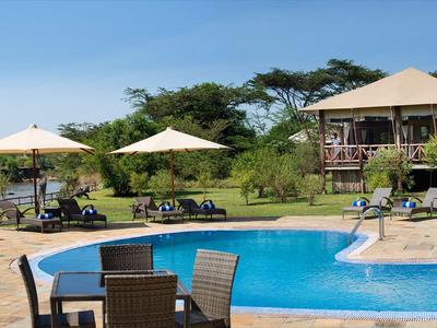 Poolbereich mit Stühlen, Sonnenschirmen und Hütten in einer grünen Hotelanlage unter blauem Himmel.