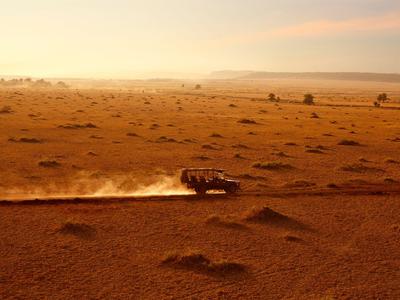 Geländewagen fährt auf staubiger Sandpiste in weitläufiger Wüstenlandschaft bei Sonnenuntergang.