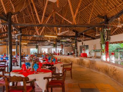 Großer, offener Restaurantbereich mit Strohdach, Holzmöbeln und rot-weißen Tischdecken.