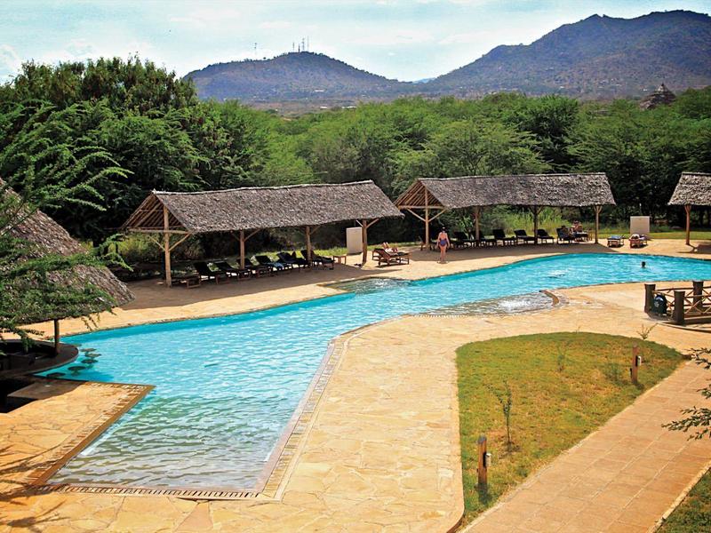 Piscina del hotel con cascadas, rodeada de tumbonas y pabellones frente a montañas y paisaje boscoso.
