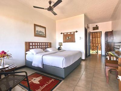 Bright hotel room with two single beds, ceiling fan, and wooden furniture.