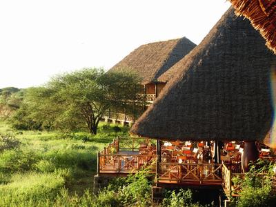 Open restaurant with thatched roof surrounded by green vegetation in sunlight.