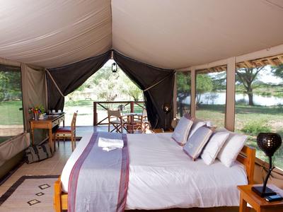 A comfortable bed in a luxury tent overlooking nature and water.