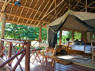 Covered porch with wooden railing, table, and chair next to a safari tent with bed.