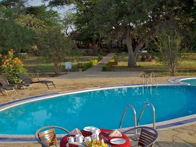 A garden table with a red cloth and breakfast beside a pool in a green landscape.