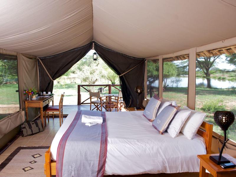 A comfortable bed in a luxury tent overlooking nature and water.