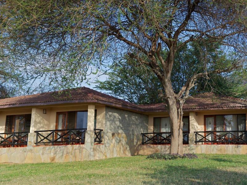 Two stone bungalows with covered verandas in a green, tree-filled setting.
