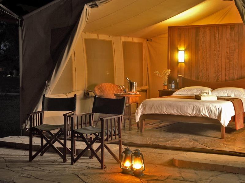 Lit tent with beds and chairs on a terrace at night.