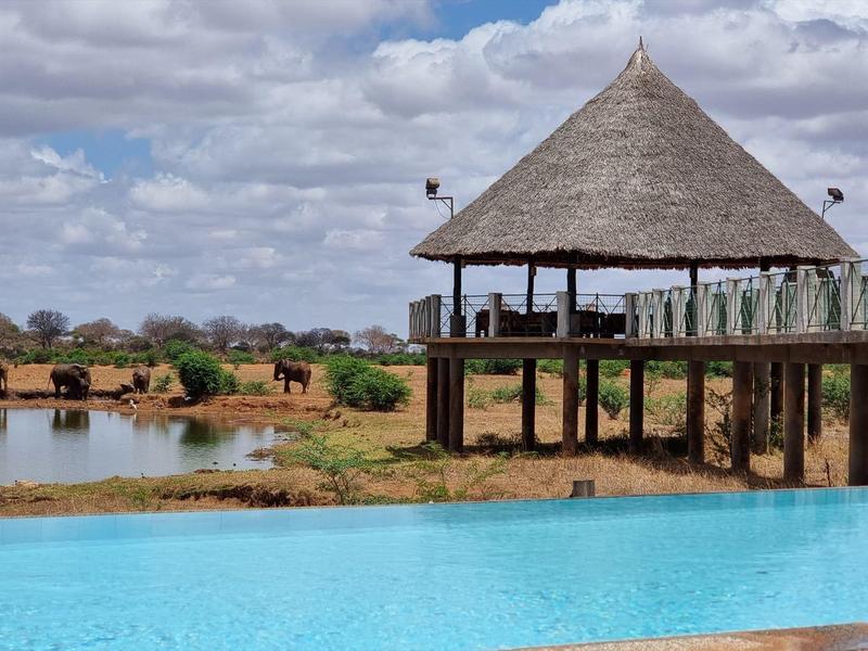 Infinity pool overlooking an African lodge by a river and hilly landscape.