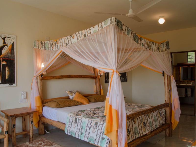 Wooden bed with mosquito net and colorful bedding in a bright hotel room.