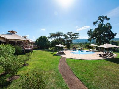 Ein sonniger Hotelgarten mit Pool, Liegestühlen und Sonnenschirmen unter blauem Himmel.