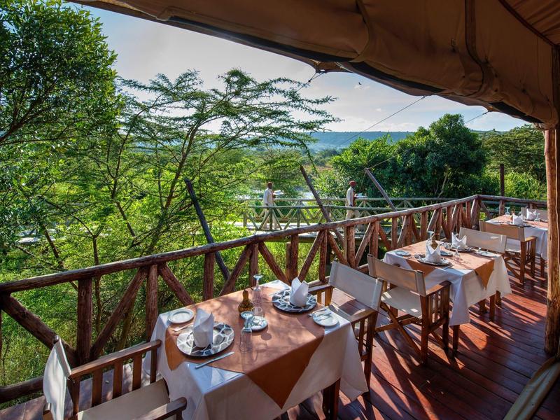 Terrasse mit gedeckten Tischen und Blick auf grüne Bäume und Hügel im Hintergrund