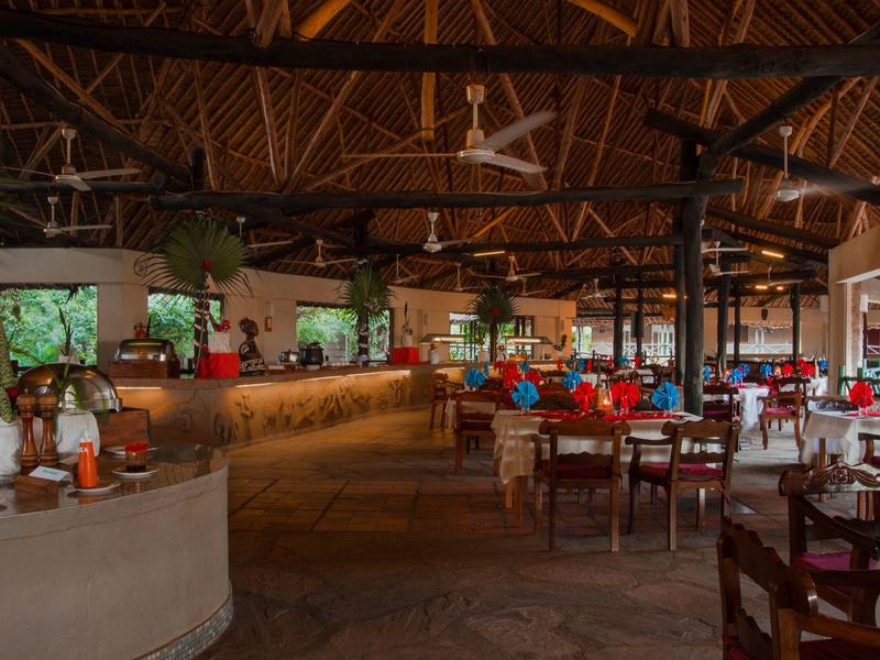 Restaurante amplio con techo de madera y ventiladores, mesas con flores rojas y decoración tropical.