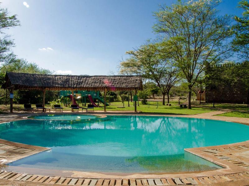 Piscina al aire libre en un paisaje verde con árboles y un pabellón al fondo.